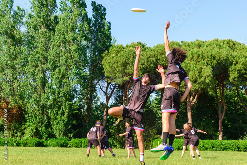 Group of young teenagers people in team wear playing a frisbee game in park oudoors. jumping man catch a frisbee to a teammate in an ultimate frisbee match. milennials friends outside in a garden