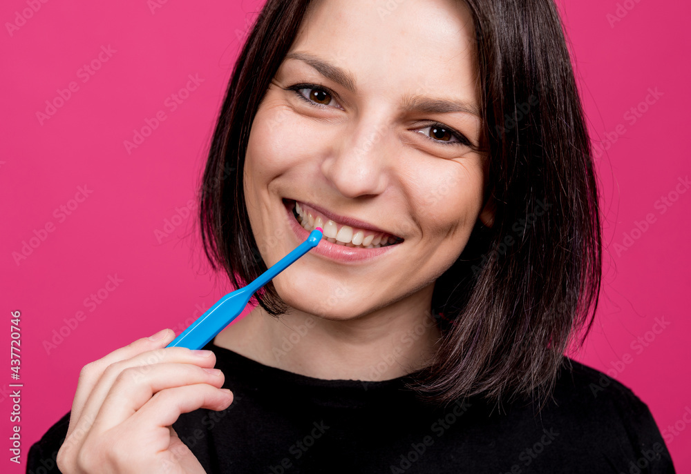 Beautiful happy young woman with single tufted toothbrush on blank pink background