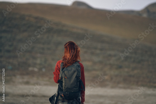 red-haired traveler with a backpack looks back on the nature in the mountains