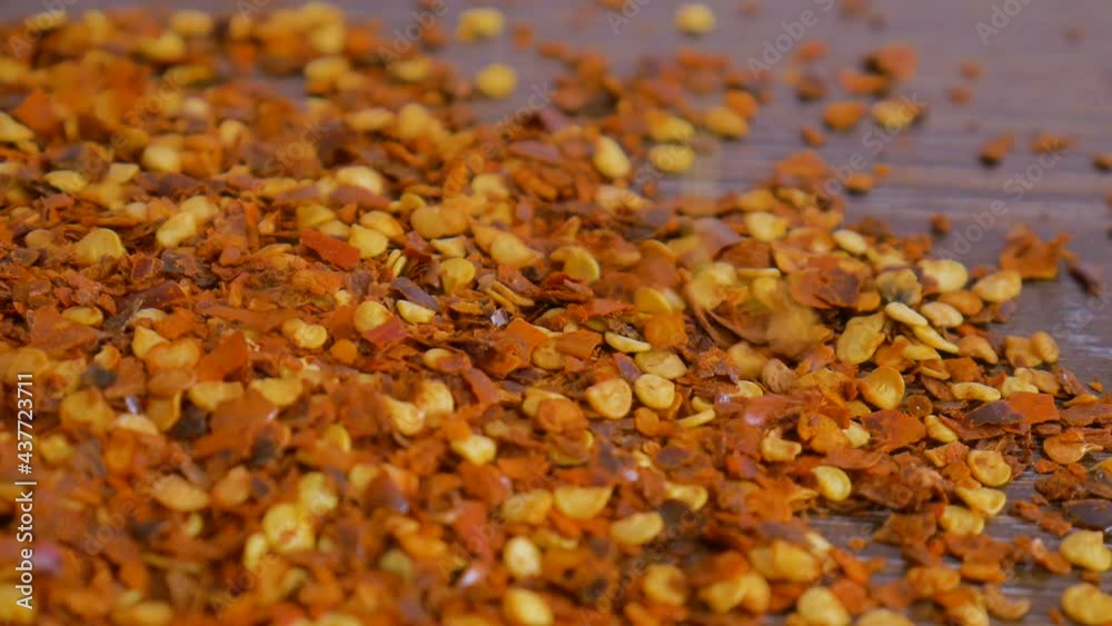 Red hot chili pepper flake falling down on wooden table. Cooking concept, seasonings for food, close up Red hot chili pepper flake falling down on wooden table. Cooking concept, seasonings for food, close up