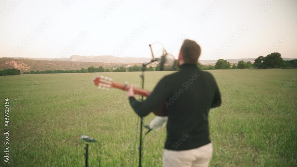 Rear view of male singer playing guitar on grass field in nature during beautiful weather. Out of focus,bokeh effect. Rear view of male singer playing guitar on grass field in nature during beautiful weather. Out of focus,bokeh effect.