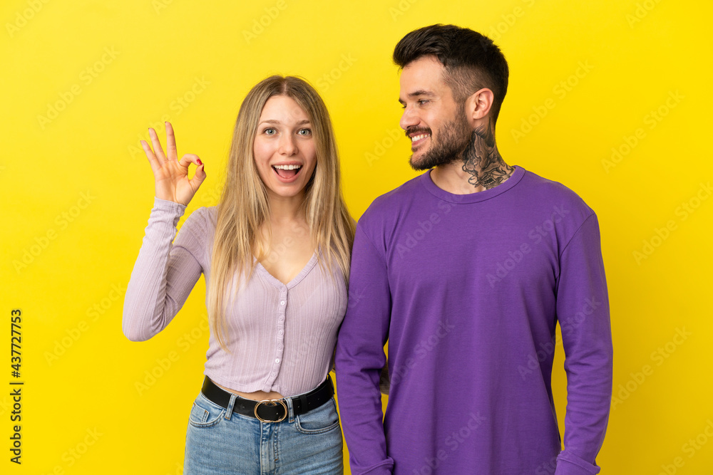 Young couple over isolated yellow background showing an ok sign with fingers Young couple over isolated yellow background showing an ok sign with fingers