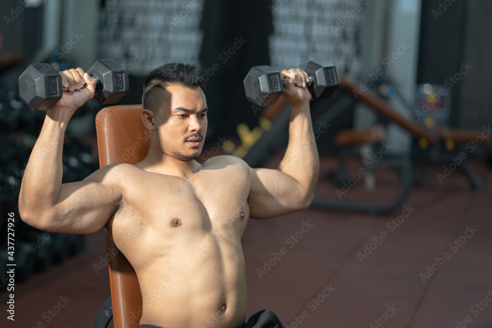 Handsome adult Asian men sweating while lift up the dumbbell workout for biceps and shoulder muscle part inside of fitness gym. Bodybuilding athlete sport training for body strength and good health. Handsome adult Asian men sweating while lift up the dumbbell workout for biceps and shoulder muscle part inside of fitness gym. Bodybuilding athlete sport training for body strength and good health.