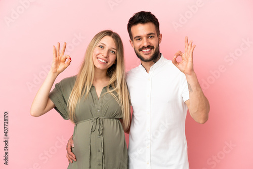 Pregnant woman and man over isolated pink background showing an ok sign with fingers