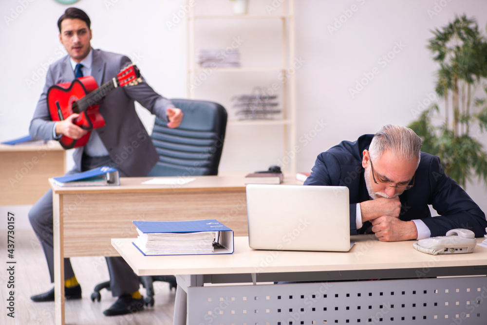 Young male employee playing guitar in the presence of old boss Young male employee playing guitar in the presence of old boss