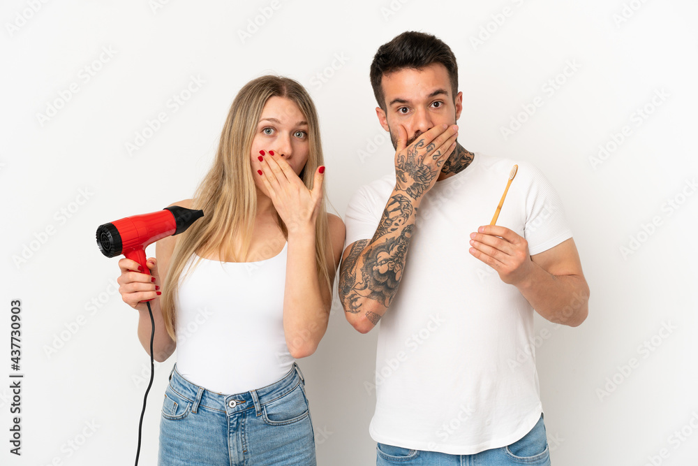 Couple holding a hairdryer and brushing teeth over isolated white background covering mouth with hands for saying something inappropriate Couple holding a hairdryer and brushing teeth over isolated white background covering mouth with hands for saying something inappropriate