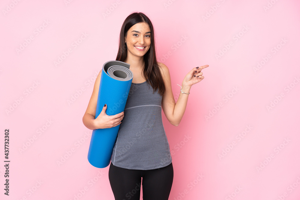 Young caucasian woman with mat isolated on pink background pointing finger to the side Young caucasian woman with mat isolated on pink background pointing finger to the side