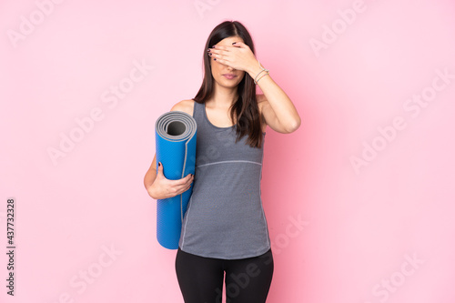 Young caucasian woman with mat isolated on pink background covering eyes by hands
