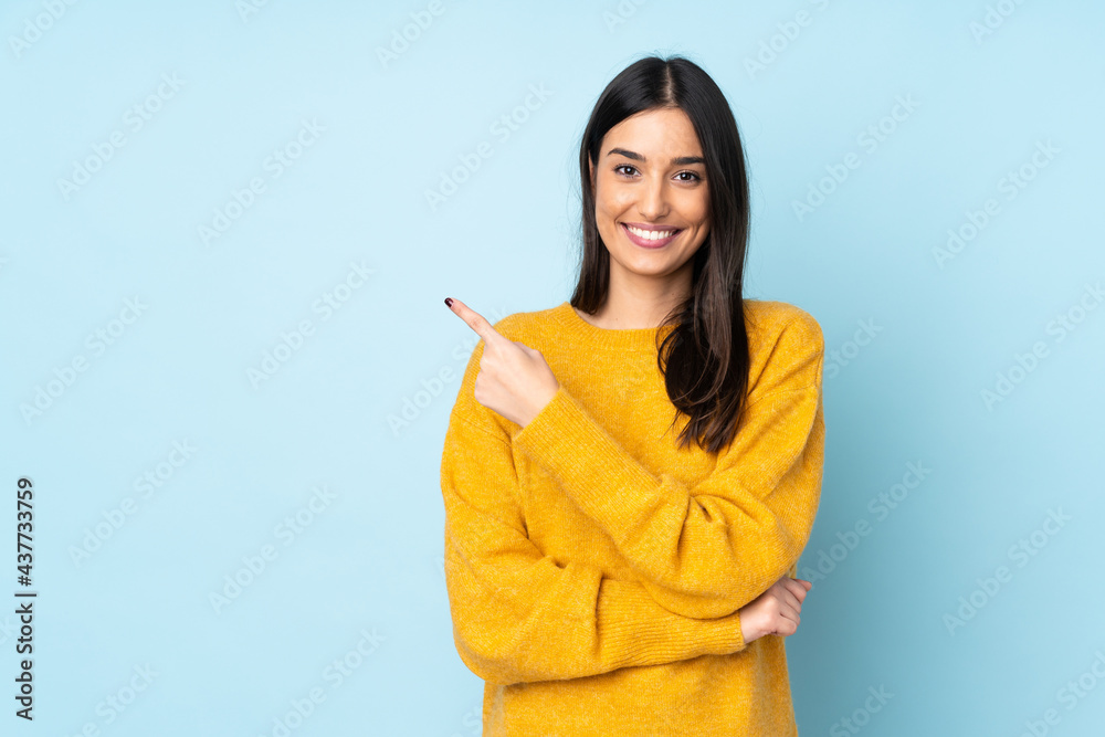 Young caucasian woman isolated on blue background pointing to the side to present a product - obrazy, fototapety, plakaty 