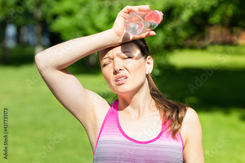 hot summer weather. girl covering her head from sunshine with hand in pain. young woman with bottle of water from thirst on sun. female female go sports get heat and sunstroke. Headache, feeling bad photo