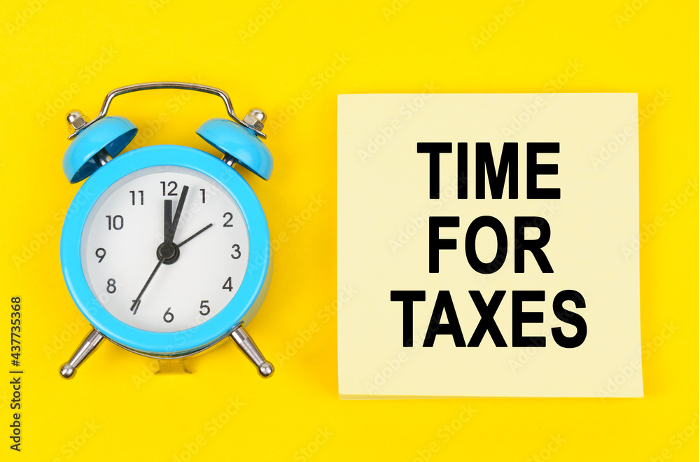 On a yellow background lie a clock and a sticker sheet with the inscription - TIME FOR TAXES On a yellow background lie a clock and a sticker sheet with the inscription - TIME FOR TAXES