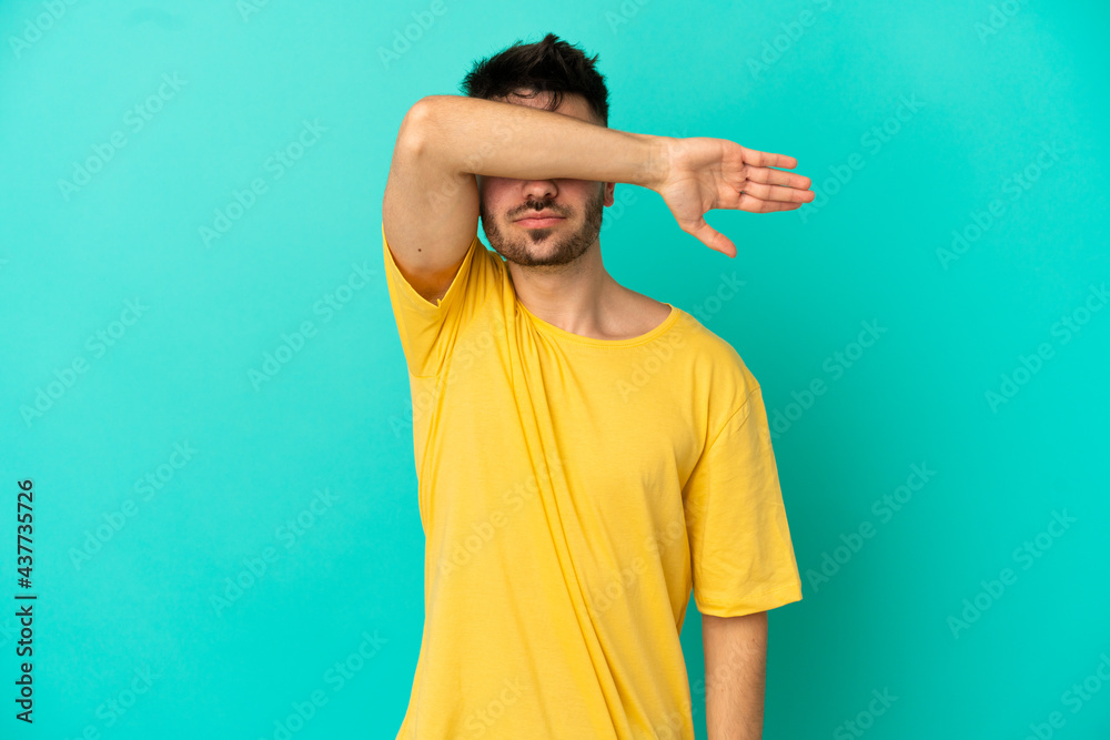 Young caucasian man isolated on blue background covering eyes by hands Young caucasian man isolated on blue background covering eyes by hands