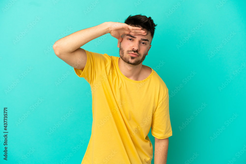 Young caucasian man isolated on blue background looking far away with hand to look something Young caucasian man isolated on blue background looking far away with hand to look something