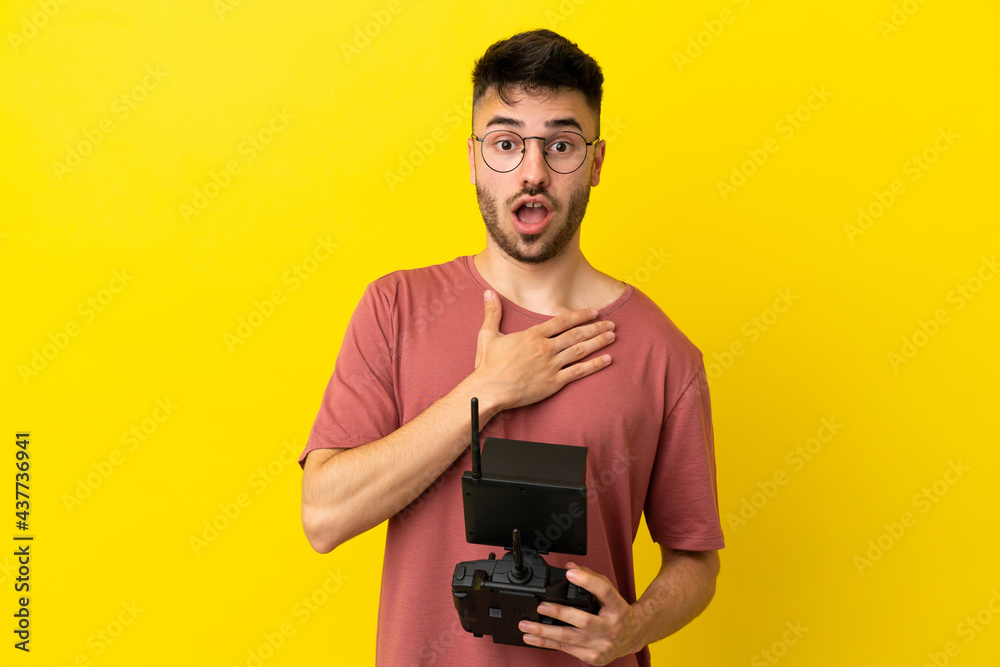 Man holding a drone remote control isolated on yellow background surprised and shocked while looking right Man holding a drone remote control isolated on yellow background surprised and shocked while looking right