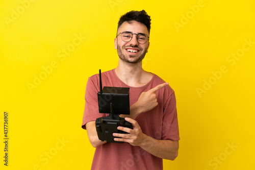 Man holding a drone remote control isolated on yellow background pointing to the side to present a product