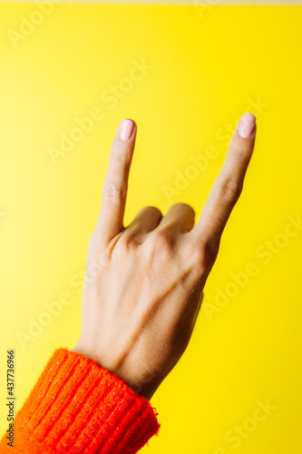 Woman's hand in red sweater shows rockstar gesture on yellow background