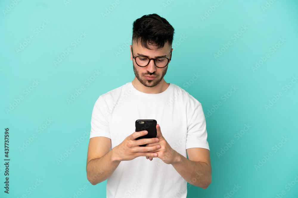 Young caucasian man isolated on blue background using mobile phone Young caucasian man isolated on blue background using mobile phone