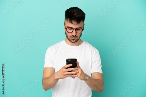 Young caucasian man isolated on blue background using mobile phone © luismolinero