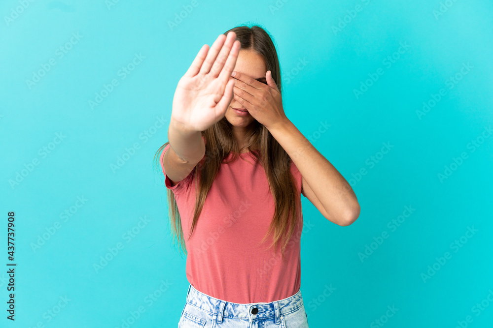 Young woman over isolated blue background making stop gesture and covering face Young woman over isolated blue background making stop gesture and covering face
