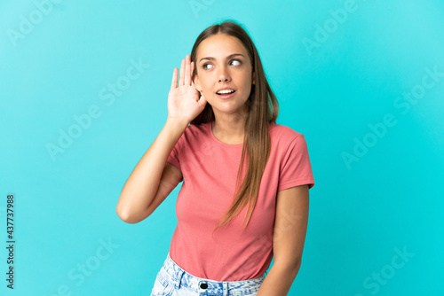 Young woman over isolated blue background listening to something by putting hand on the ear