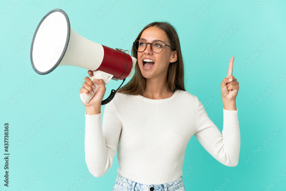 Young woman over isolated blue background shouting through a megaphone to announce something in lateral position Young woman over isolated blue background shouting through a megaphone to announce something in lateral position