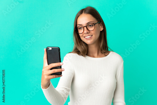 Young woman over isolated blue background making a selfie with mobile phone
