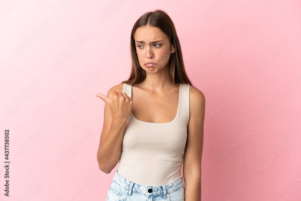 Young woman over isolated pink background unhappy and pointing to the side Young woman over isolated pink background unhappy and pointing to the side