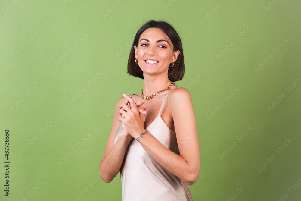 Fototapeta premium Woman in silk golden dress, huge golden necklace and earrings on green background posing
