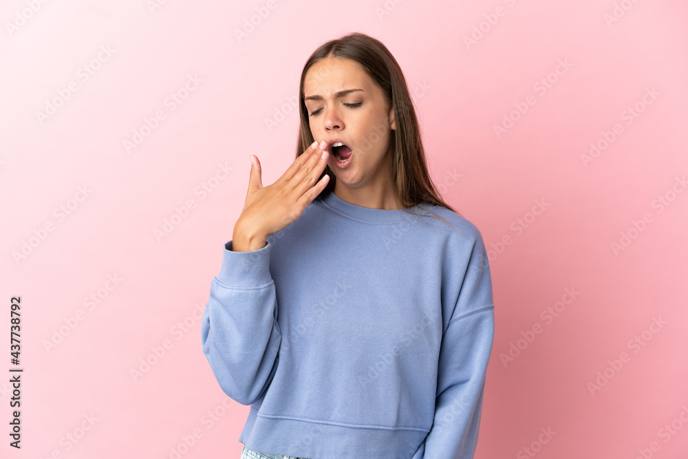 Young woman over isolated pink background yawning and covering wide open mouth with hand Young woman over isolated pink background yawning and covering wide open mouth with hand