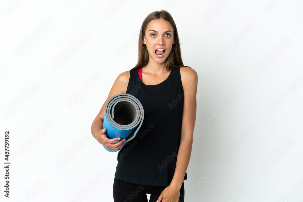 Sport woman going to yoga classes while holding a mat over isolated white background with surprise facial expression Sport woman going to yoga classes while holding a mat over isolated white background with surprise facial expression