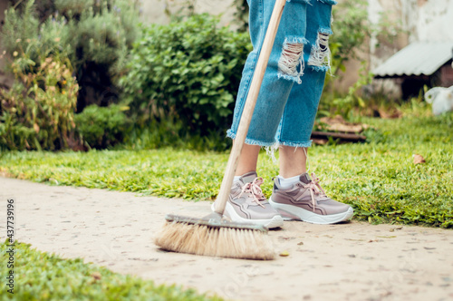image of a girl's feet holding a broom while sweeping in the yard of her house.