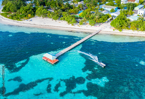 Aerial view of a motorboat leaving a wooden pier on the tropical islnd with a coral lagoon