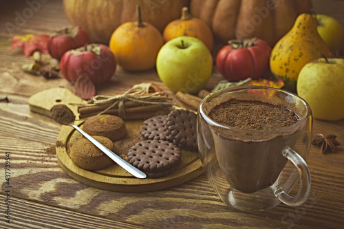 Hot cocoa, cookies and autumn harvest on wooden table. Ripe pumpkins, apples, fall leaves and persimmons on background. Coffee with chocolate chips. Concept of Christmas, Thanksgiving and Halloween.