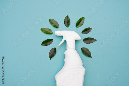 Plastic spray bottle for safe cleaning and green leaves around the bottle on a blue background. Natural organic cleaning agent. Eco-friendly cleaning spray. Eco concept of house cleaning. copy space. 