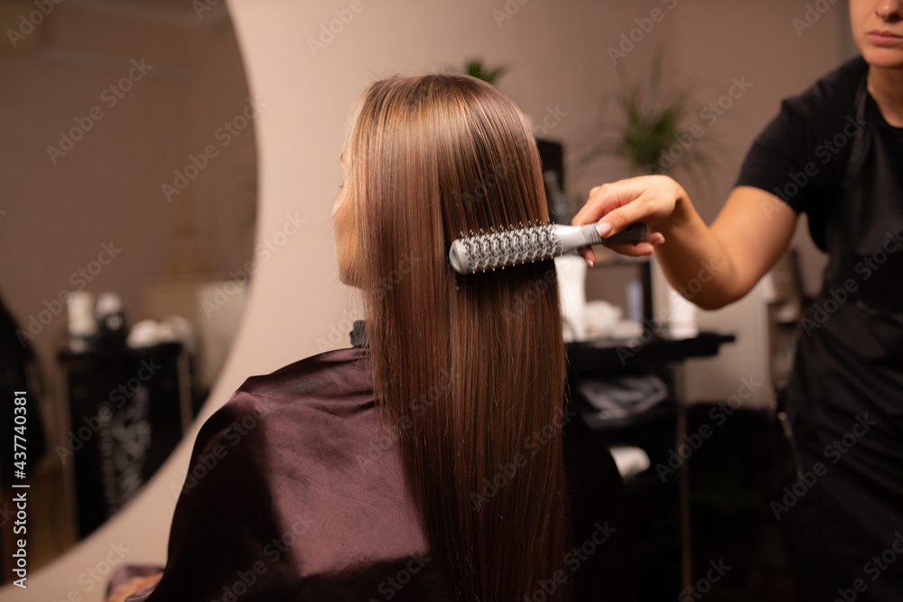 Naklejka premium coloring hair, Hair dyeing. Young professional hairdresser applies hair dye to a female client.