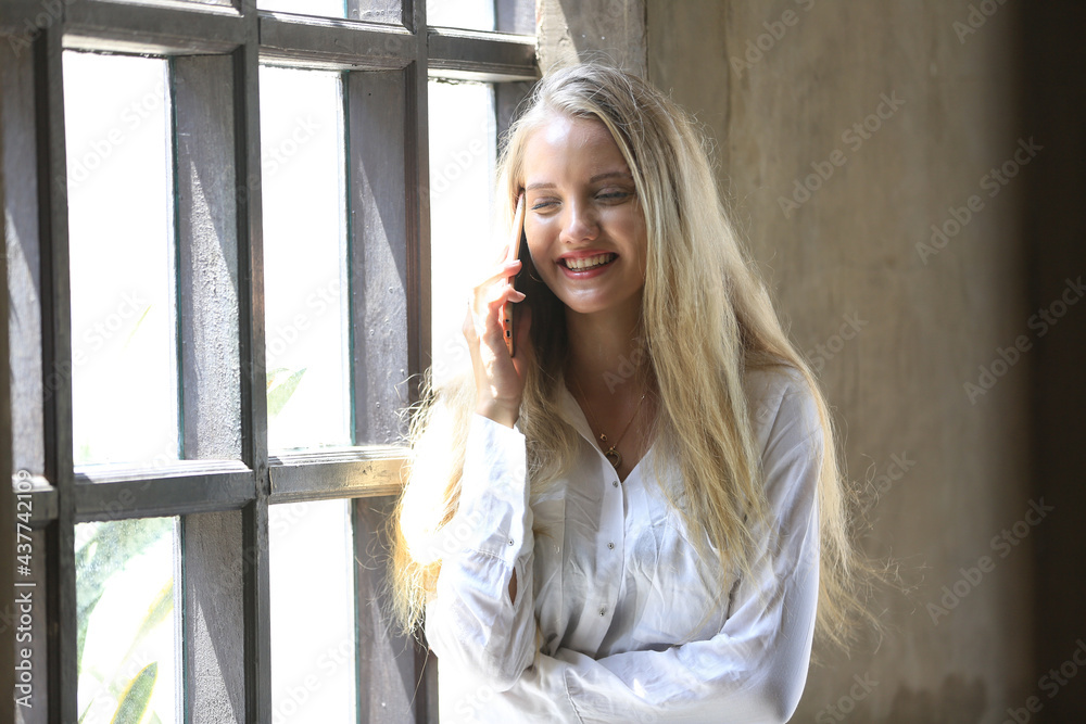 Beautiful blonde hair girl speaking on mobile phone with laptop on table outside coffee shop.