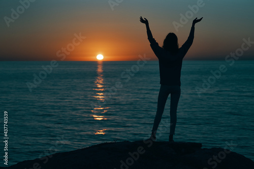 silhouette of a woman at sunset near the sea gesturing with hands back view