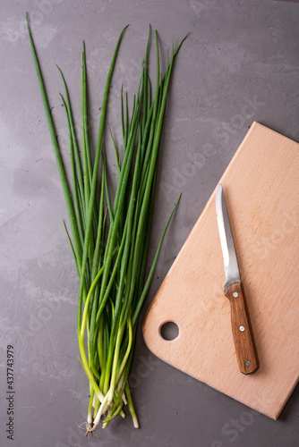 Bunch of fresh green onions with cutting board on gray background, healthy food, vegetarianism.