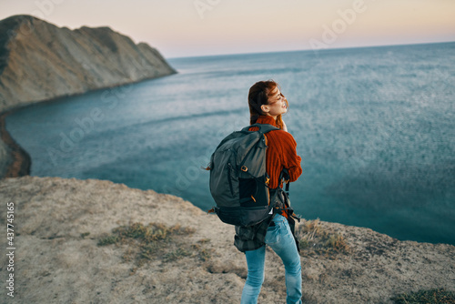 traveler in a red sweater and jeans with a backpack in the mountains near the sea top view