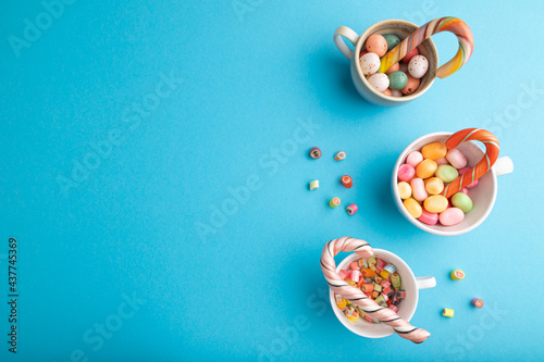 Heap of multicolored caramel candies in cups on blue pastel background. copy space, top view.