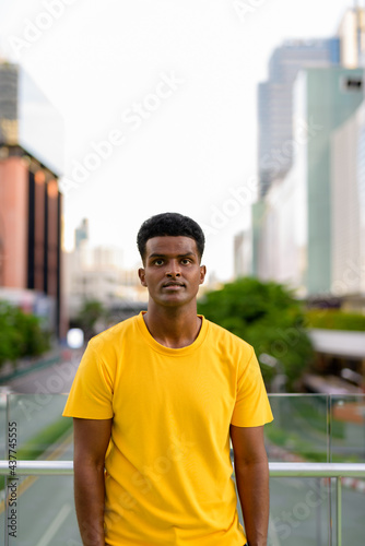 Vertical portrait of handsome black African man wearing yellow t-shirt outdoors in city