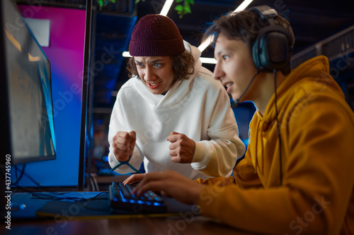 Two young gamers looks on monitor in gaming club