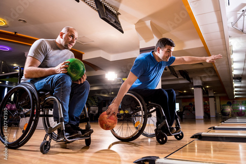 Two young disabled men in wheelchairs playing bowling in the club