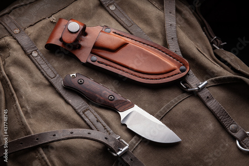 A hunting knife with a wooden handle and a leather case on a khaki canvas backpack. Weapons for self-defense and survival.
