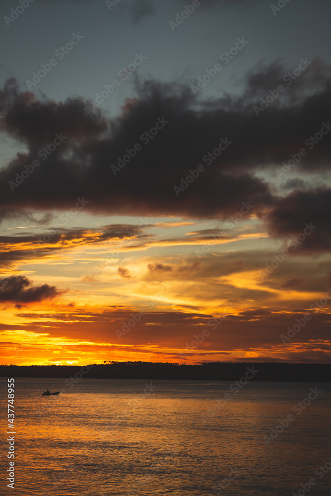 Fine art photography of a vibrantly colored sunset on the lagoon. Small silhouette of a boat.