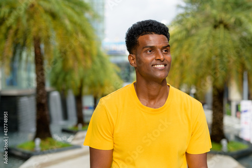 Happy black African man wearing yellow t-shirt outdoors in city during summer while smiling and thinking
