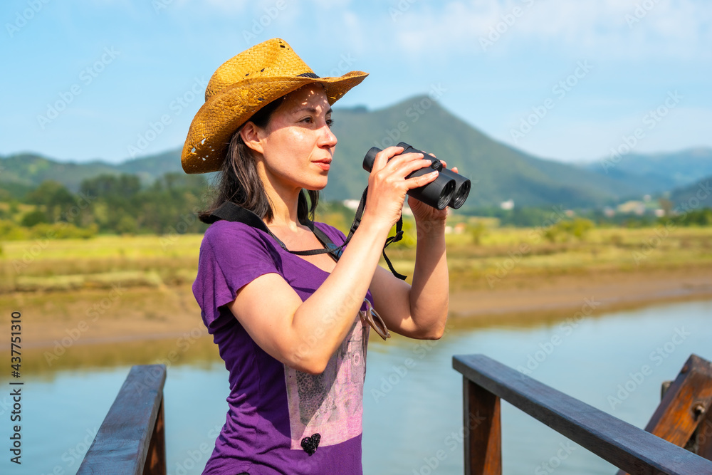 A young tourist looking at birds with spyglasses from the wooden piers of the Urdaibai marshes, a biosphere reserve in Bizkaia next to Mundaka. Basque Country