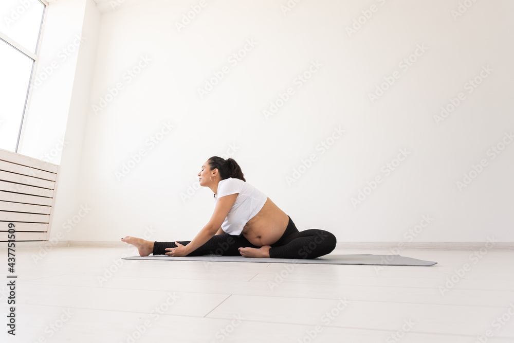 Young flexible pregnant woman doing gymnastics on rug on the floor on white background. The concept of preparing the body for easy childbirth. Copy space. Young flexible pregnant woman doing gymnastics on rug on the floor on white background. The concept of preparing the body for easy childbirth. Copy space.