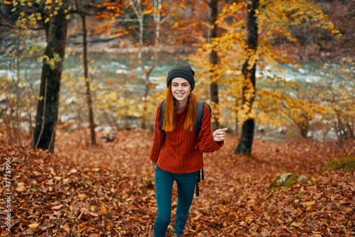 woman hiker with backpack in autumn forest near mountain river and fallen leaves