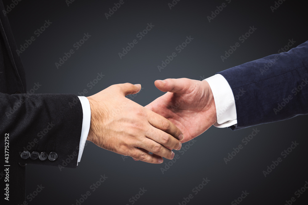 Handshake of two businessmen on a black wall background, partnership concept, close up
